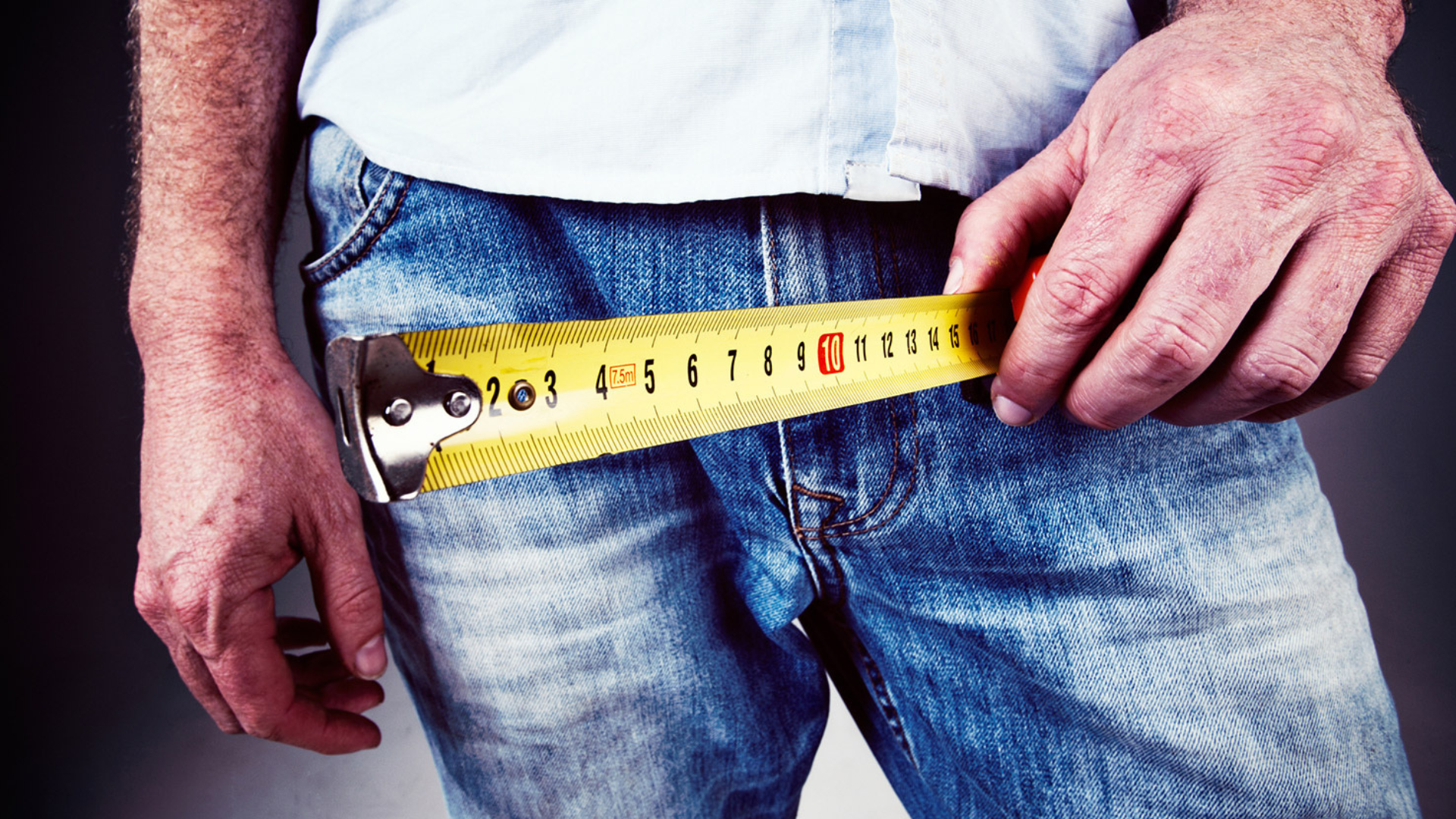 A man wearing denim pants while holding a tape measure