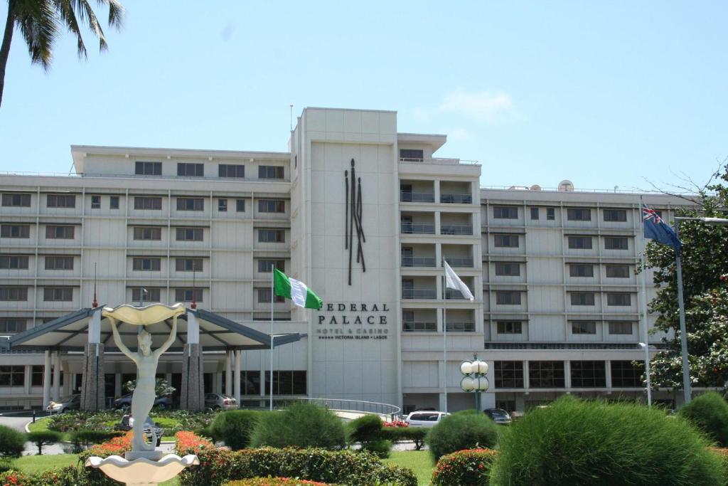 The Federal Palace Hotel entrance, featuring a shell-shaped sculpture, with cars parked, and Nigerian flag