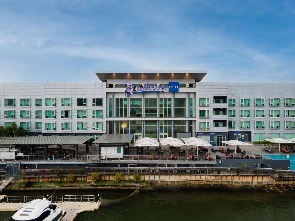 Radisson Blu hotel entrance with glass front, riverside patio, and “Radisson BLU” sign against blue sky