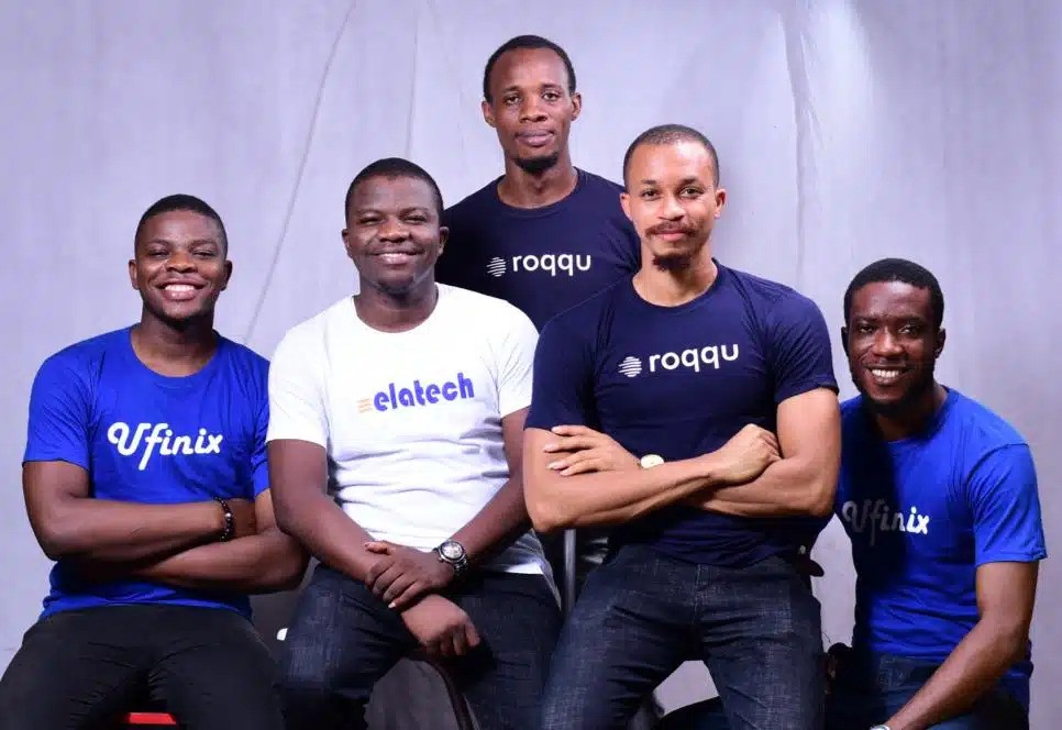Four men in blue shirts smiling and posing together for a group photo