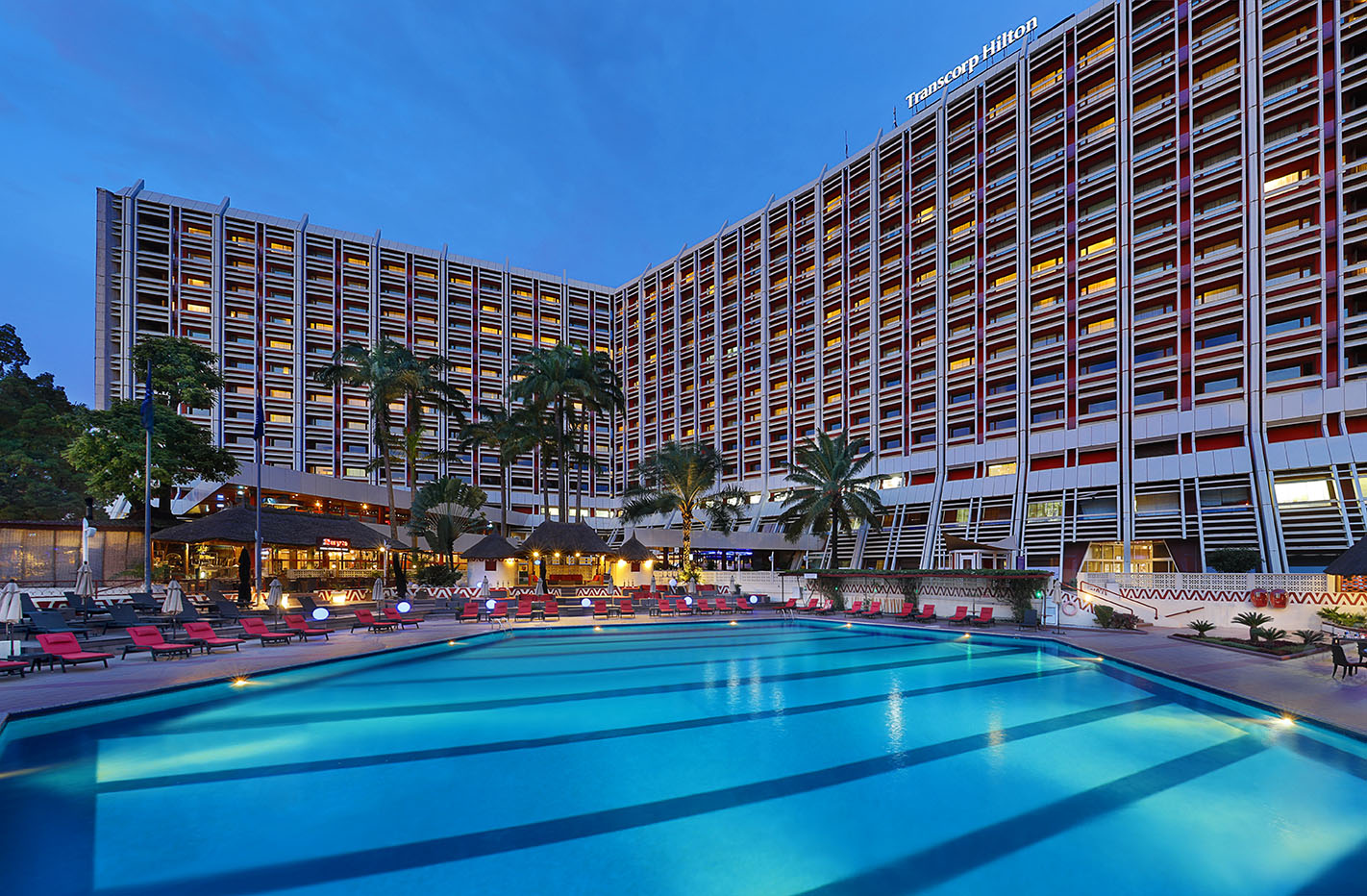 Poolside area of the Transcorp Hilton at night, with red loungers and warm lights reflecting on the water