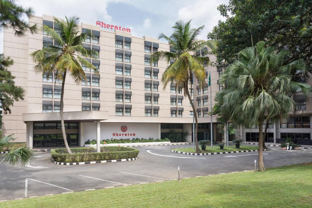 Sheraton hotel entrance with palm trees, manicured hedges, and a curved driveway under a partly cloudy sky