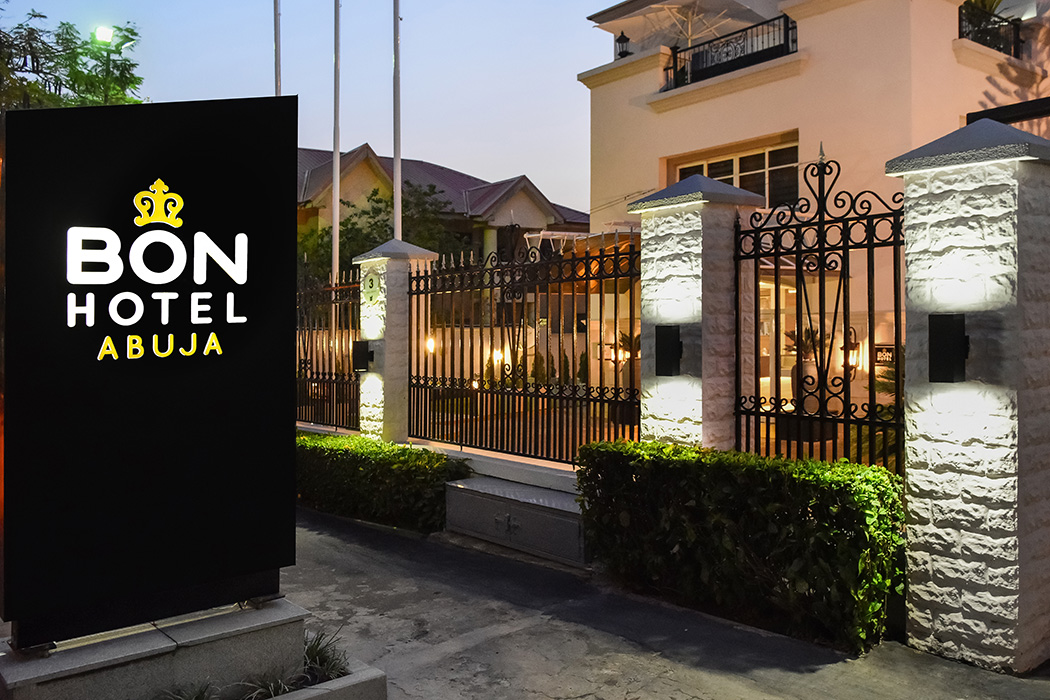 Bon Hotel Abuja entrance at dusk, featuring a lit sign, ornate gate, and stone pillars with warm lighting