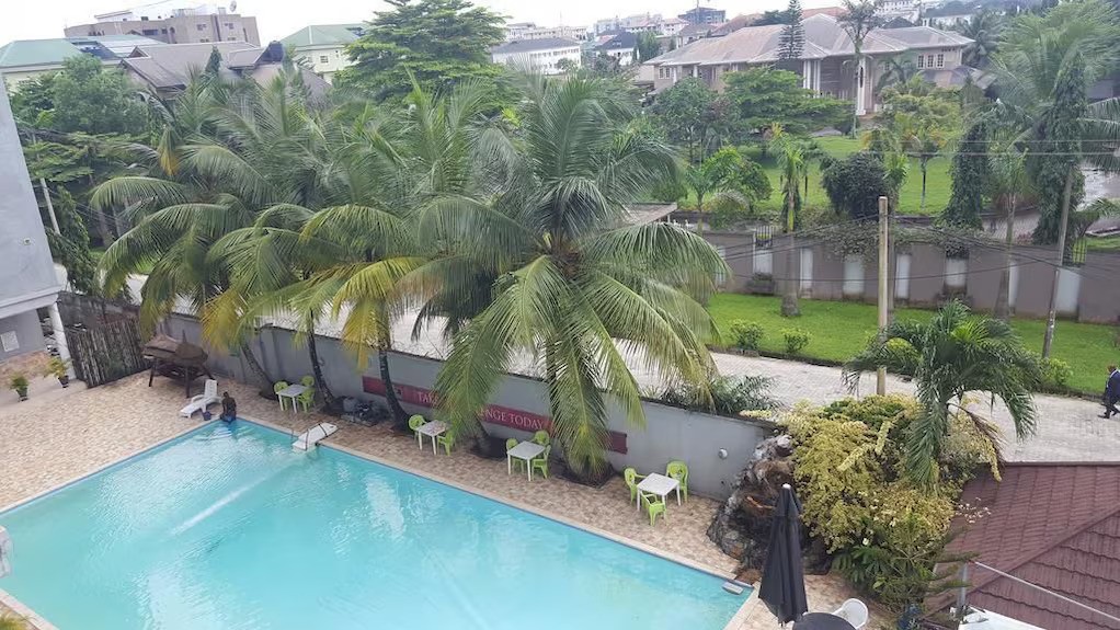 Outdoor pool surrounded by palm trees, green chairs, and a sandy deck in the Bougainvillea Hotel